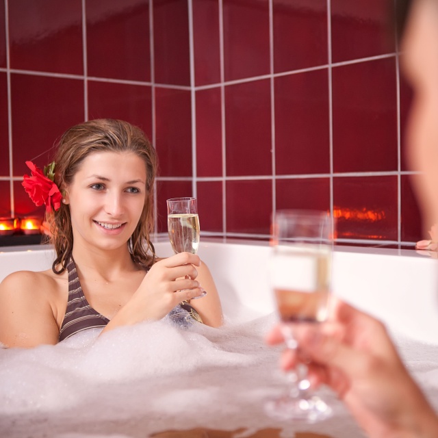 Sie sehen zwei Personen mit Sektgläsern in einer Badewanne.