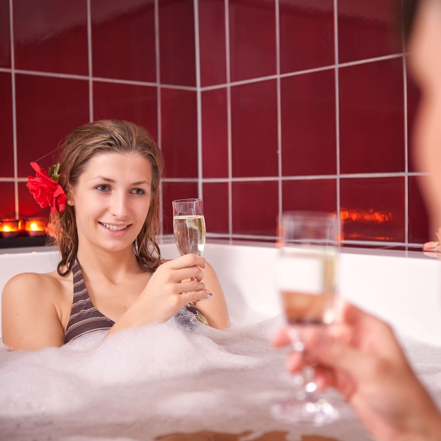 Sie sehen zwei Personen mit Sektgläsern in einer Badewanne.